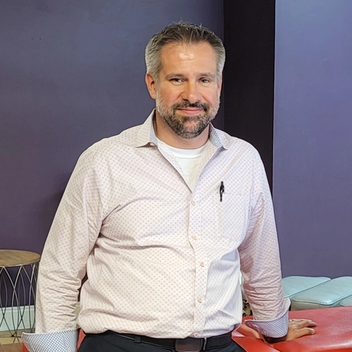 Dr. Steve Ranicki smiling in front of a purple wall.